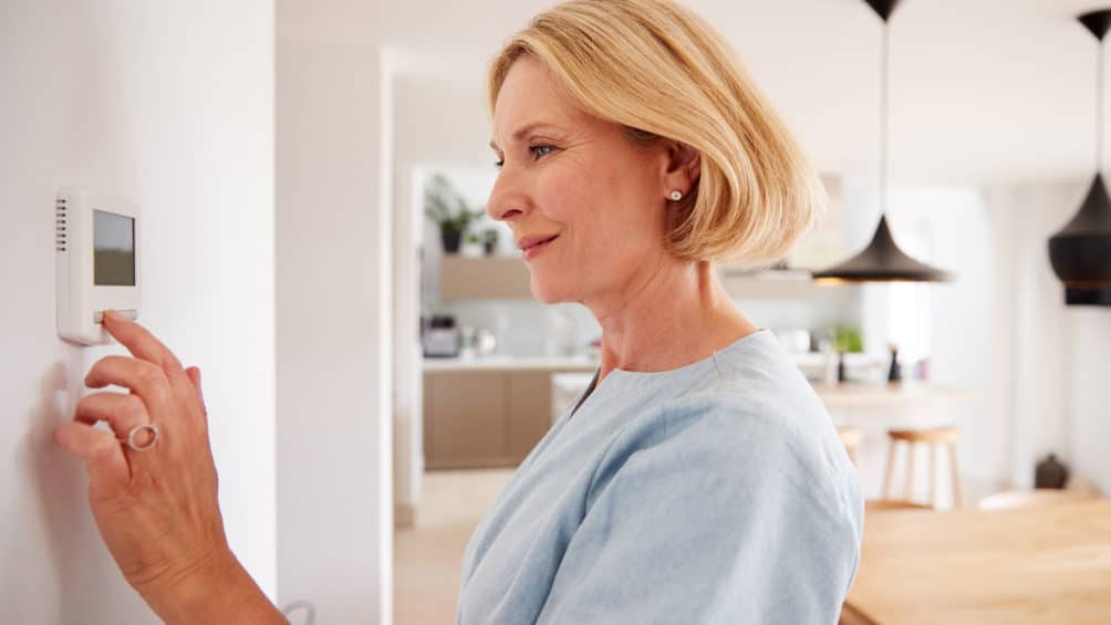 A homeowner adjusts their thermostat, kicking on the air conditioning and cooling down their home.
