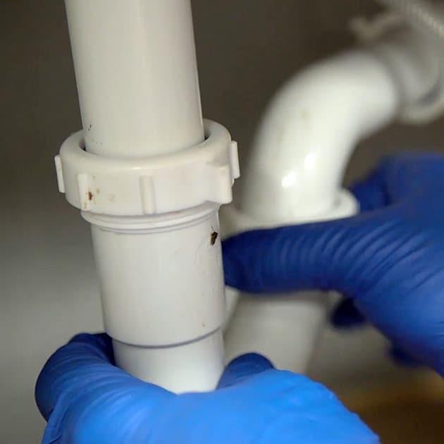 Wearing protective blue gloves, one of our plumbers attaches two pieces of PVC drain pipe together.