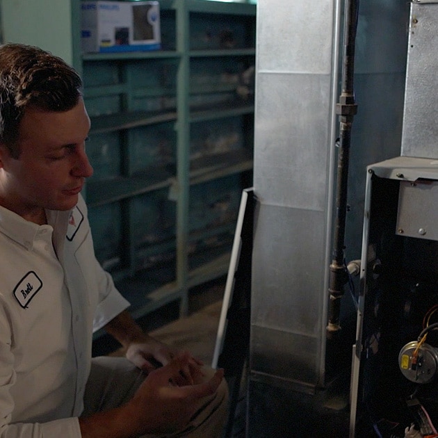 A Reimer heating repair technician re-installs the front panel of this gas furnace after completing repairs.