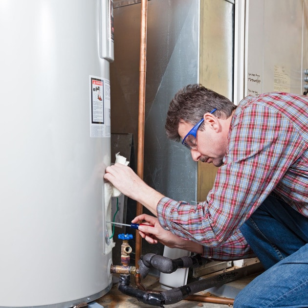 A Reimer plumber uses a screwdriver to finish up maintenance for this home's water heater.