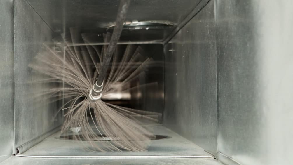 Our IAQ specialist uses a cleaning tool to clear out an air duct ahead of installing one of our air-purifying air scrubbers.