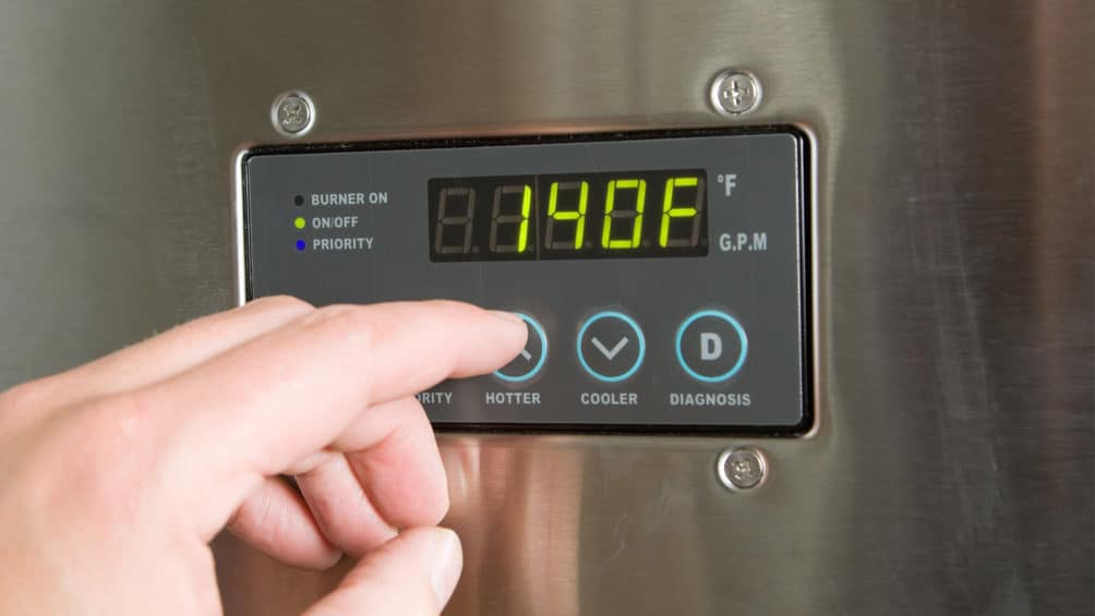 A Reimer plumber uses a control panel to adjust the temperature of this tankless water heater after installation.